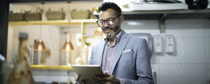 A smartly dressed small business owner checking his restaurant's inventory on a tablet.