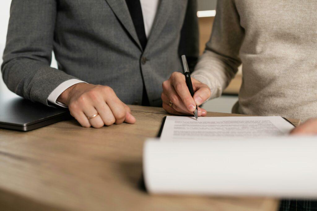 A borrower signs a loan document as a lender employee looks on.