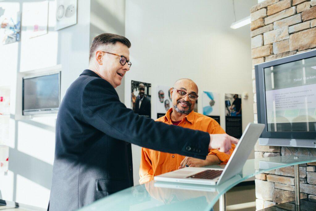 A lender points at a computer screen as a small business owner looks on.