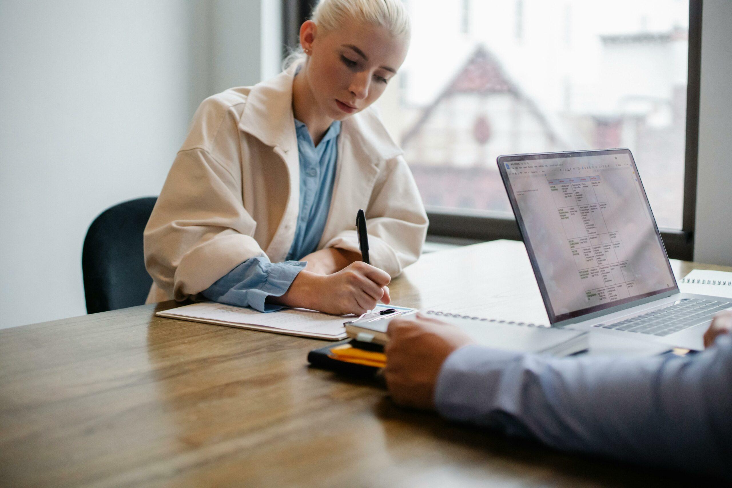 A lender and borrower have a meeting about the loan. The borrower is writing something on a clipboard.