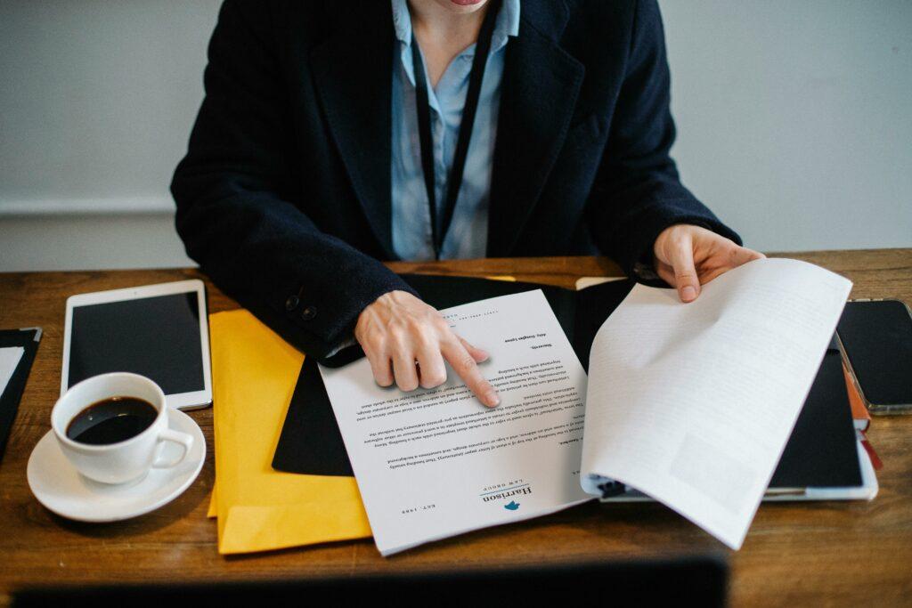 lender-employee-pointing-papers A lender employee who has been analyzing a stack of papers has turned to a specific page and is pointing at a specific piece of information.