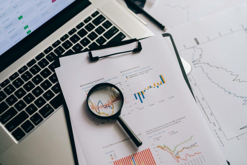A laptop and papers showing business finances, along with a magnifying glass. Signifies close analysis of business finance data.