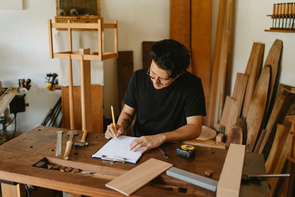 The owner of a carpentry business writes something on a clipboard in their workshop.