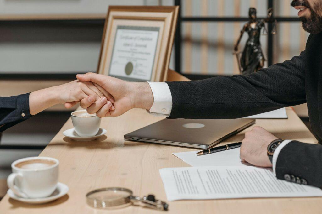 business-agreement-handshake Two businesspeople shake hands at a meeting with a contract and pen on the table between them, signifying a business agreement.