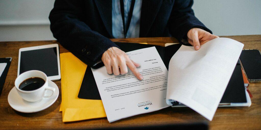 lender-employee-pointing-papers-3 A lender employee who has been analyzing a stack of papers has turned to a specific page and is pointing at a specific piece of information.